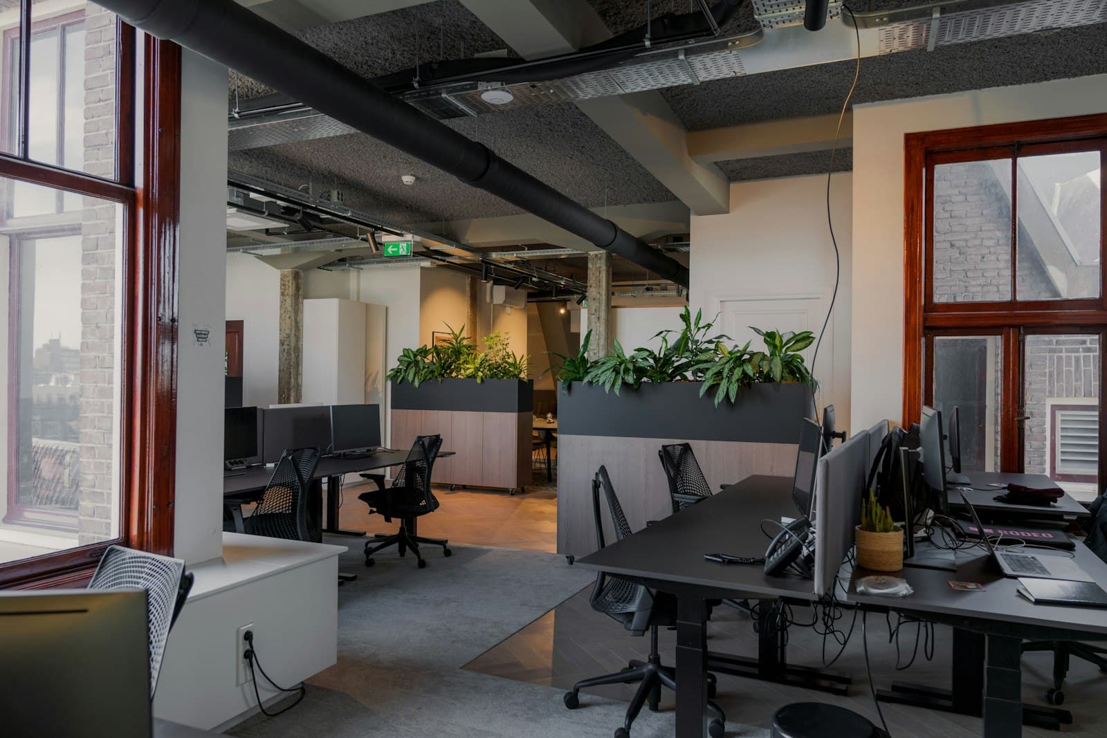 A converted-industrial office with brick, red window frames and open desks.