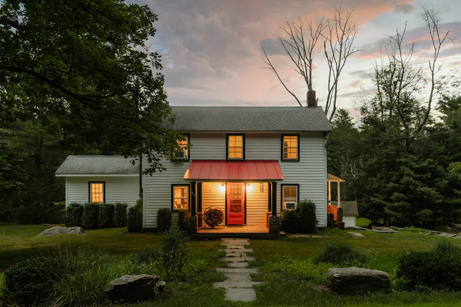 A white clapboard house at dusk with every window lit.