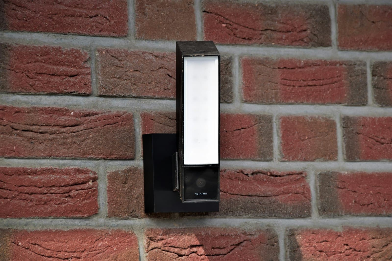 A floodlight camera mounted on a red brick wall.
