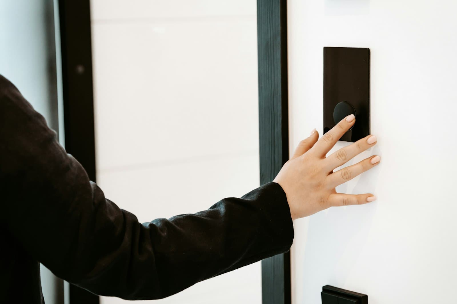 A hand reaching for a wall keypad beside a door.