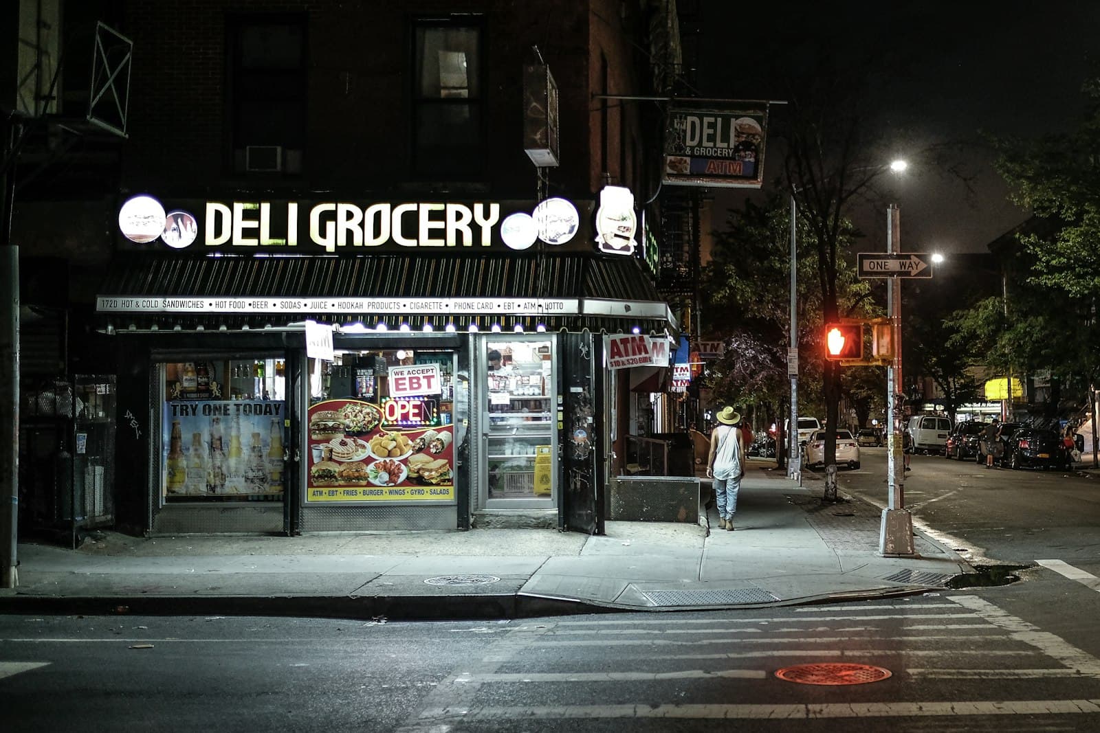 A corner deli lit up at night on a quiet New York street.