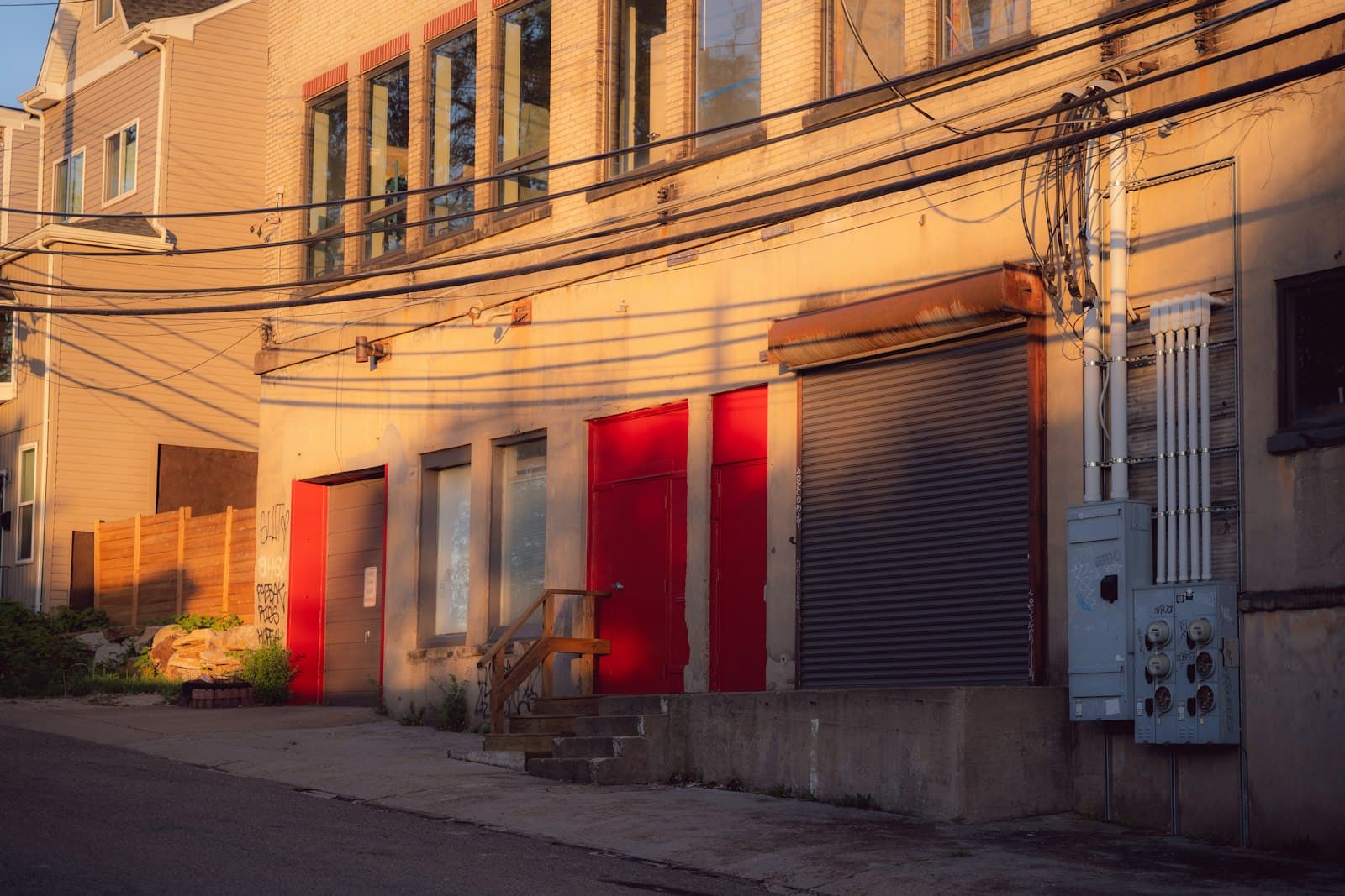 The back of a building at golden hour: red doors, a roll-down shutter and utility boxes.