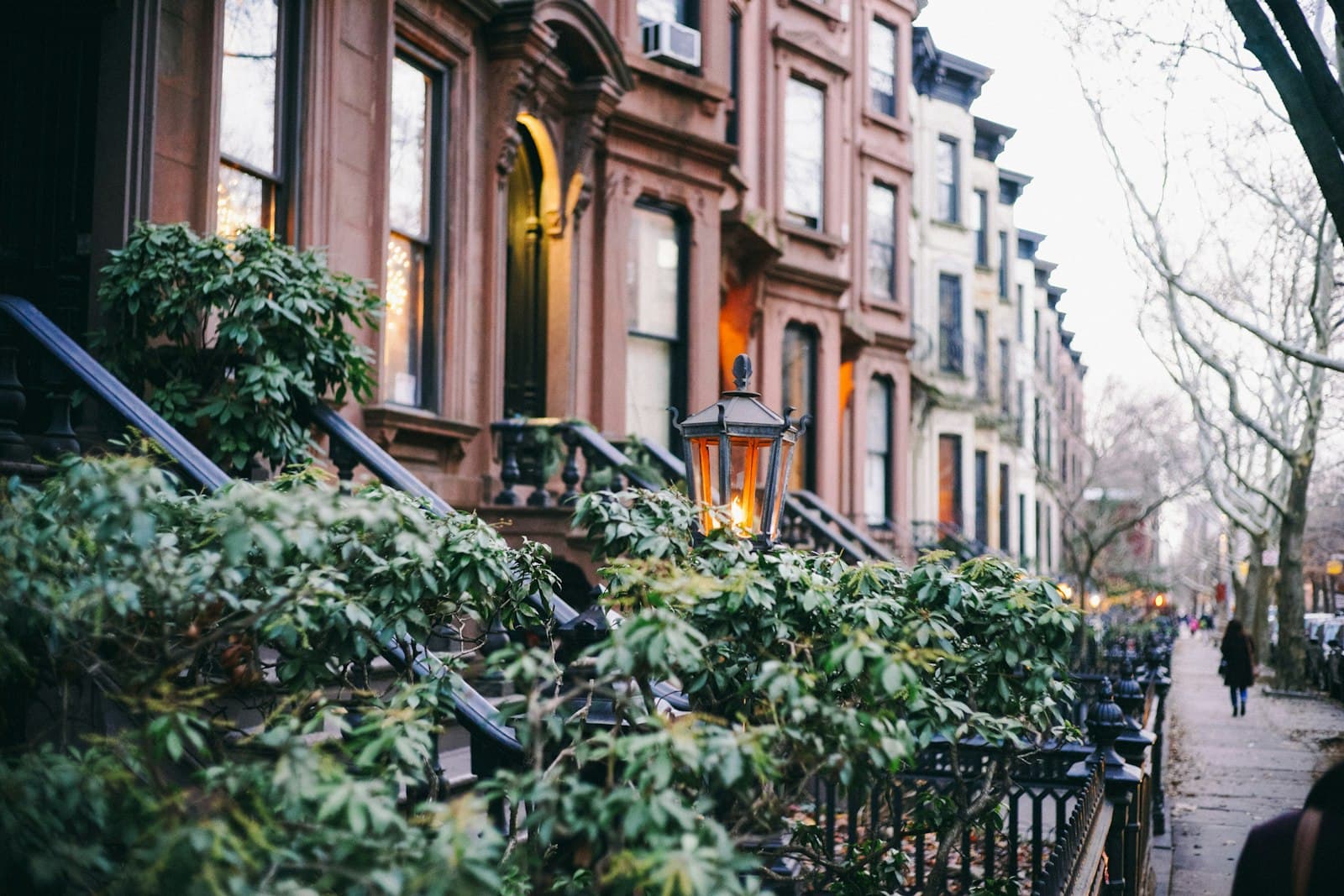 A row of Brooklyn brownstones at dusk, a stoop lamp lit.